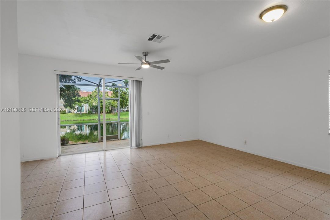 Open-concept interior featuring large-format tile flooring, a central ceiling fan, and sliding glass doors providing access to a screened-in patio overlooking a pond