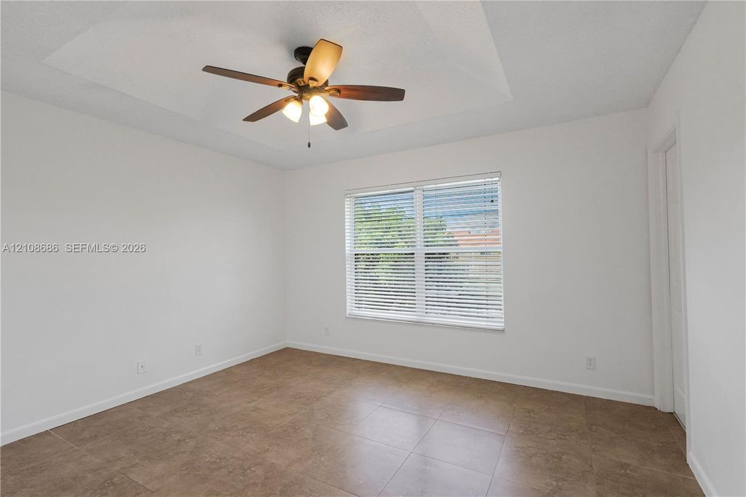 Room featuring a tray ceiling, wood-finish ceiling fan with integrated lighting, tile flooring, and a window with horizontal blinds