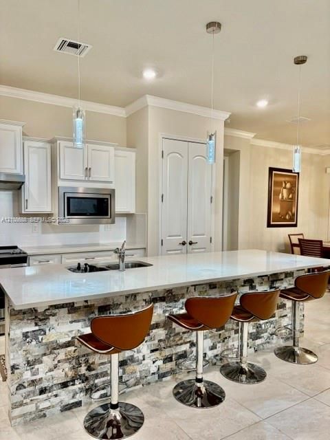 Kitchen featuring white cabinetry, solid surface countertops, a stone-veneer island facade, and triple pendant lighting