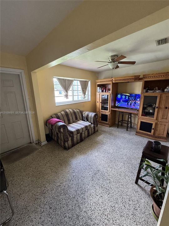 Living space featuring built-in wooden cabinetry, multi-pane window, ceiling fan with light fixture, and terrazzo flooring