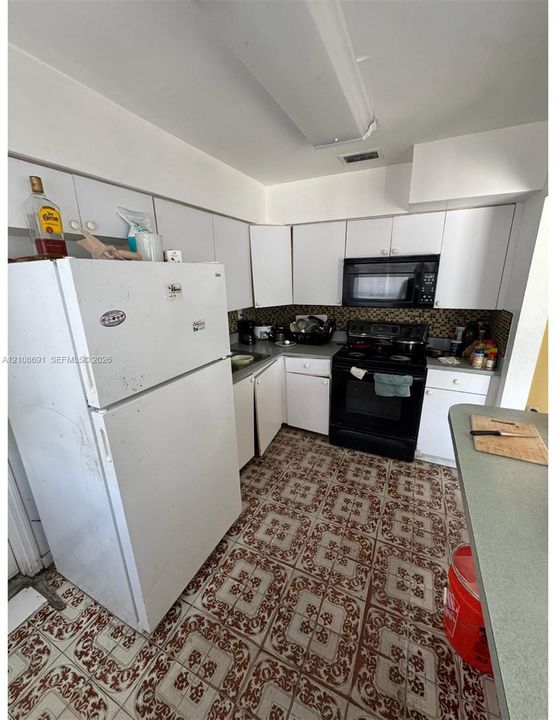 Kitchen featuring white cabinetry, patterned tile flooring, an integrated microwave, and a black range