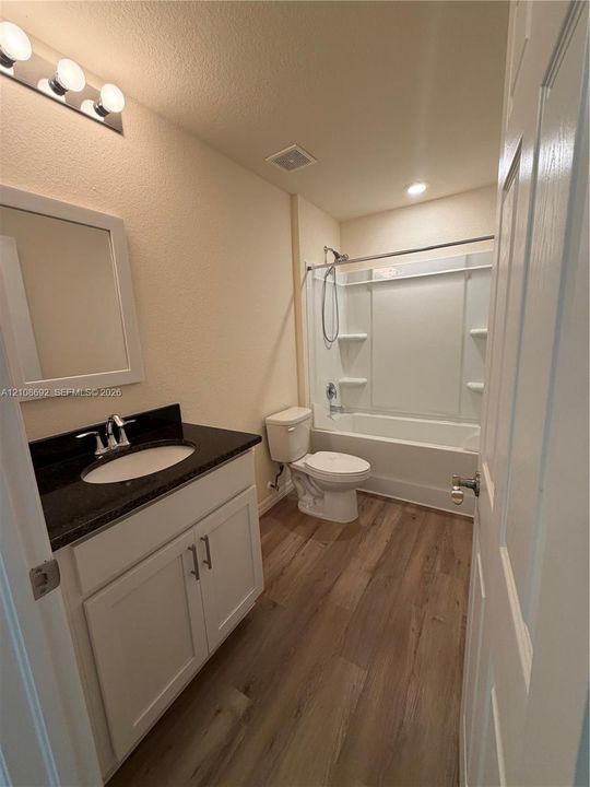Bathroom featuring a vanity with dark stone countertop, white cabinetry, wood-finish flooring, and a tub-shower combination with integrated shelving