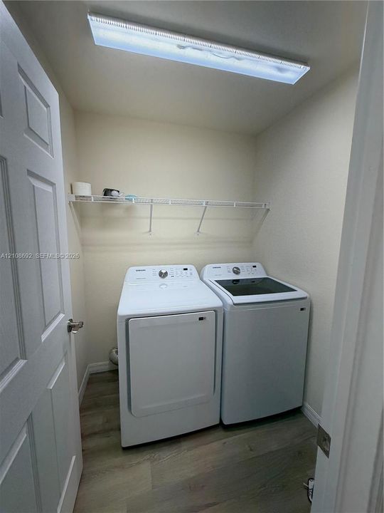 Laundry area featuring wood-finish flooring, white paneled door, and wall-mounted wire shelving