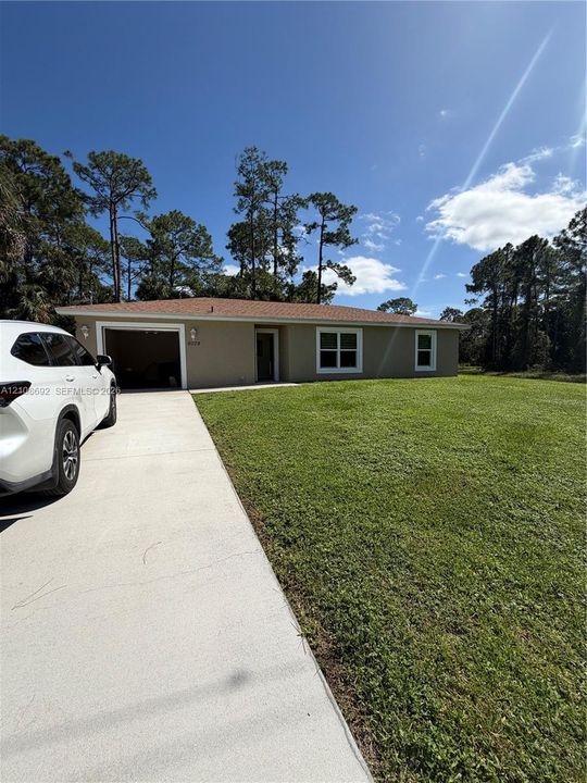 Single-story residence featuring a concrete driveway, attached garage, and expansive lawn