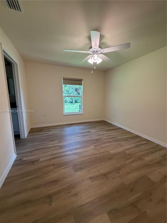 Interior room featuring wood-finish flooring, a neutral wall palette, a single-hung window with a roller shade, and a central ceiling fan with an integrated light fixture