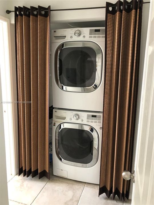 Stacked white front-load washer and dryer with chrome-finished doors, set within a recessed alcove featuring tile flooring