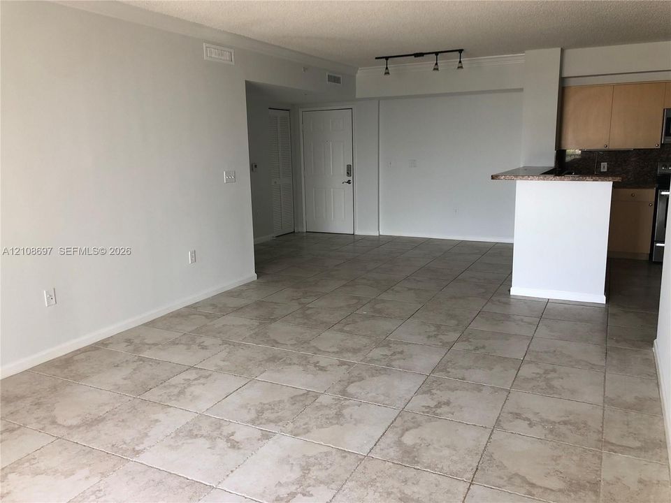 Open living area featuring neutral tile flooring, track lighting, and a kitchen peninsula with a stone-finish countertop and wood cabinetry