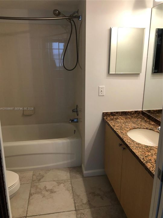 Bathroom featuring a tub-shower combination with tiled wall surround, vanity with stone-finish countertop and integrated sink, large wall-mounted mirror, and tile flooring