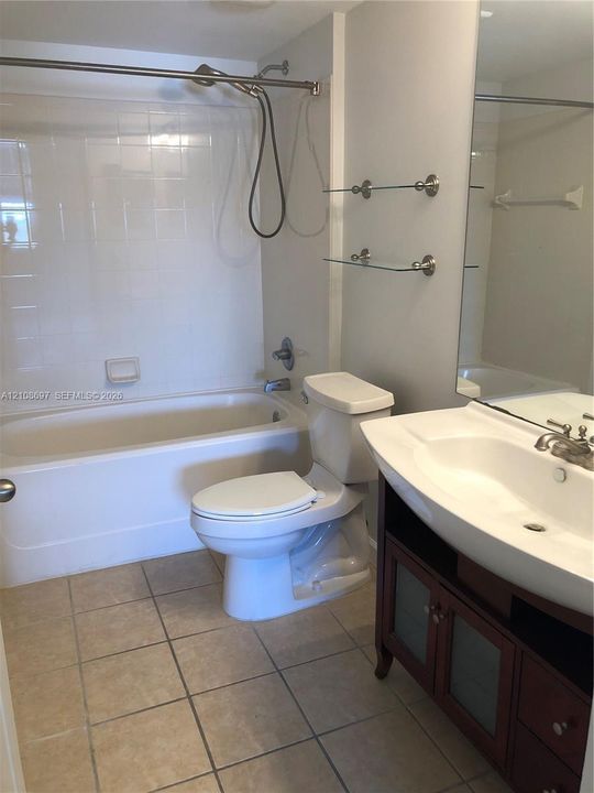 Bathroom featuring a white bathtub with a tile surround, vanity with an integrated sink, glass shelving, and tile flooring