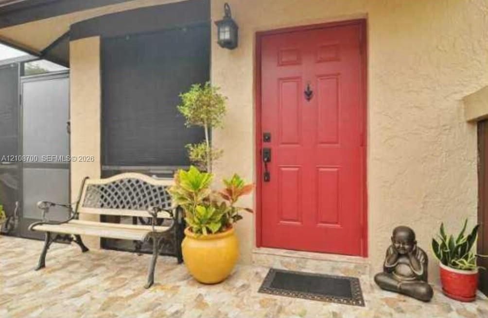 Entryway featuring a solid-panel door with a classic knocker, textured stucco exterior, stone-tile flooring, and an attached wall-mounted lantern light fixture
