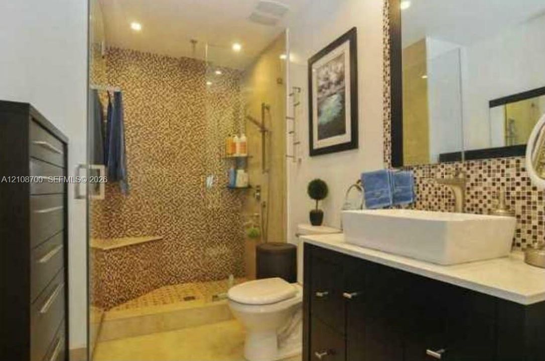 Bathroom featuring a vessel sink with a stone-surface countertop, dark cabinetry, and a walk-in shower with mosaic tile accents and a glass enclosure