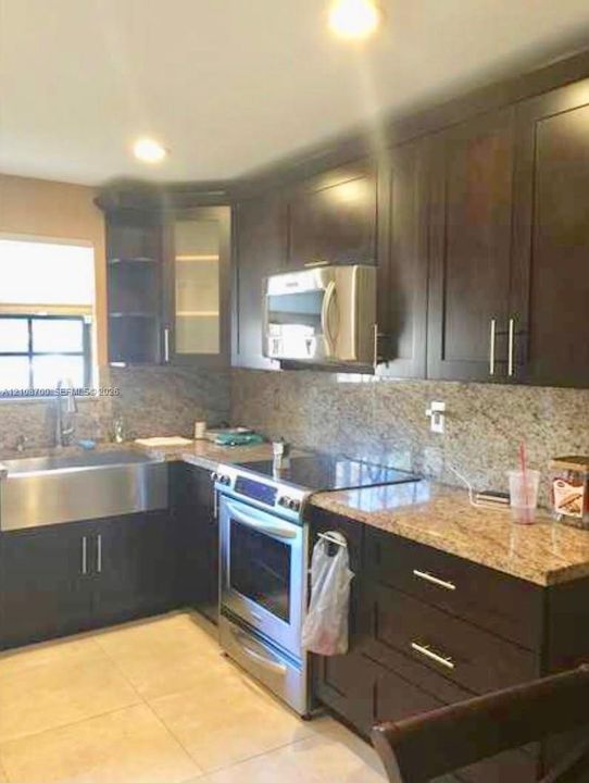 Kitchen featuring dark wood cabinetry, stainless steel apron-front sink, granite countertops, stone tile backsplash, and stainless steel appliances