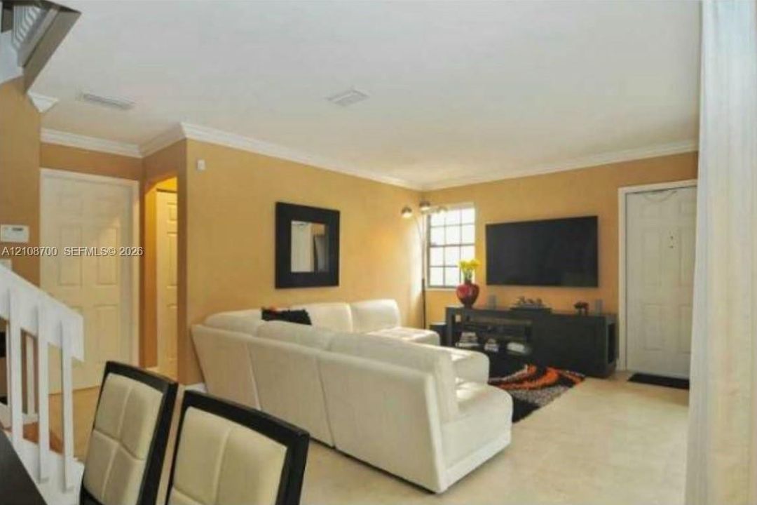 Living area featuring crown molding, neutral tile flooring, and a multi-pane window