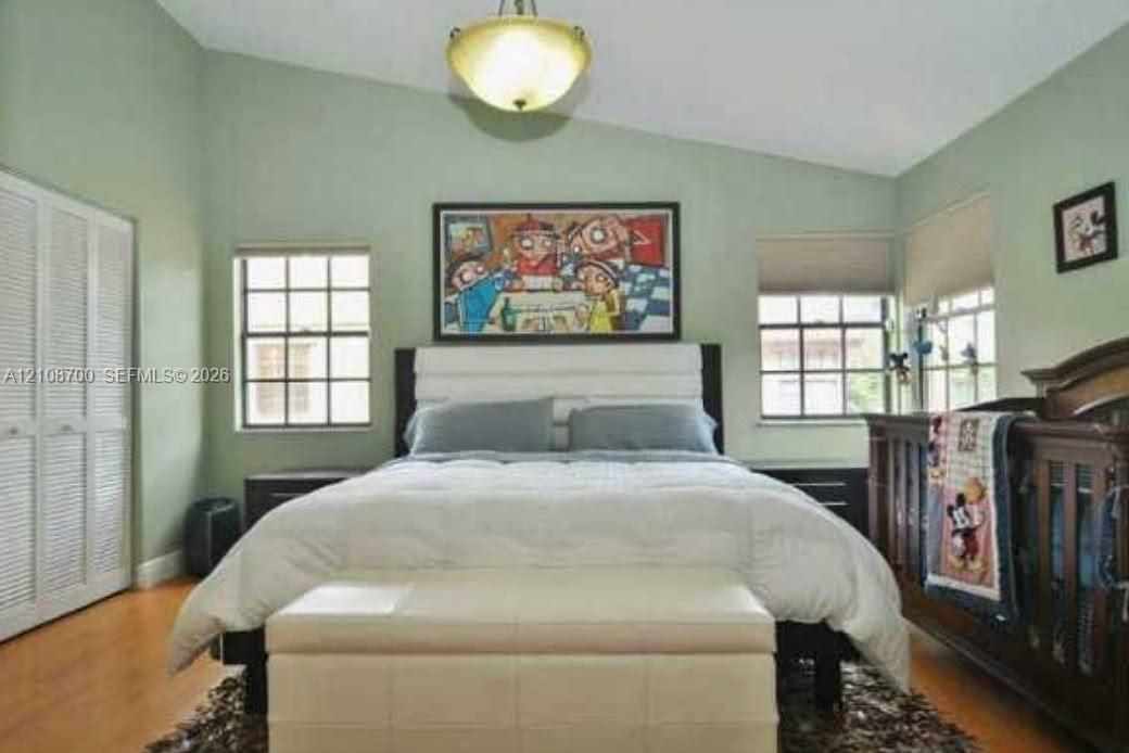 Vaulted ceiling featuring a central dome light fixture, multi-pane windows, and bi-fold closet doors with wood-finish flooring