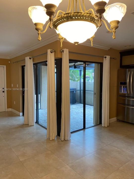 Interior space featuring large-format tile flooring, a multi-arm chandelier with glass globes, crown molding, and corner-opening sliding glass doors leading to a covered outdoor patio