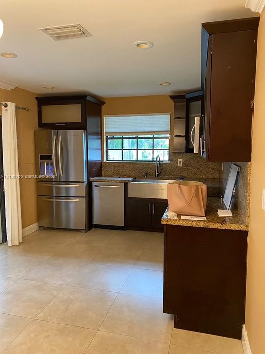 Kitchen featuring dark-finish cabinetry, stone countertops, stainless steel appliances, apron-front sink, and tile flooring