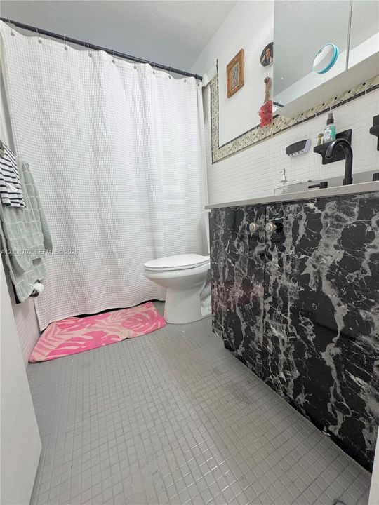 Bathroom featuring a vanity with dark patterned finish, white tile wall accents, square floor tiling, and matte black faucet fixtures