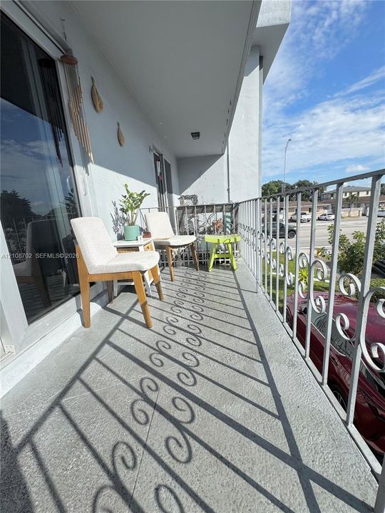 Covered balcony featuring textured concrete flooring, white metal scrollwork railing, and sliding glass door access