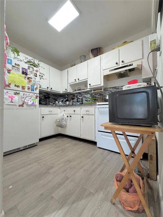 Kitchen featuring white cabinetry, wood-finish flooring, multi-toned mosaic tile backsplash, and a recessed ceiling light