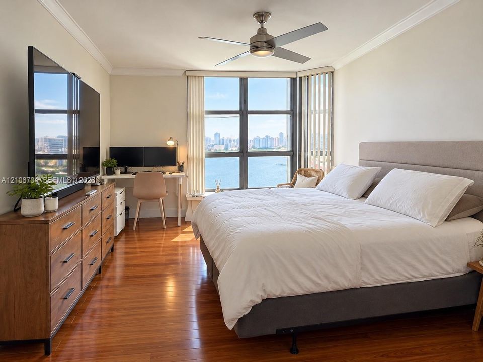 Wood-finish flooring, floor-to-ceiling windows with urban and water scenery, and a ceiling fan with integrated lighting