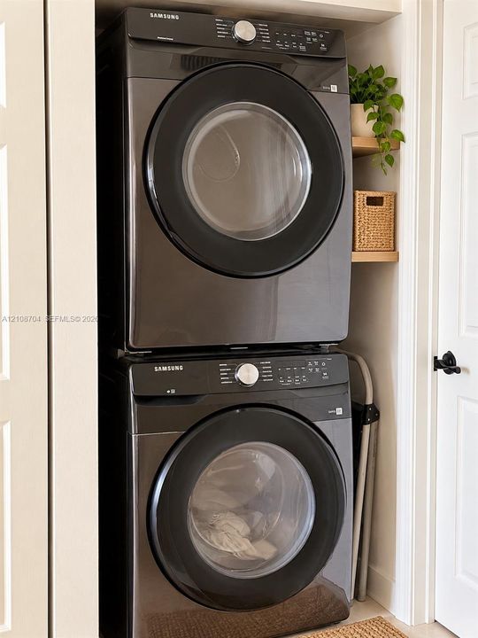 Stacked laundry center featuring dark-finish front-load appliances and built-in light wood shelving