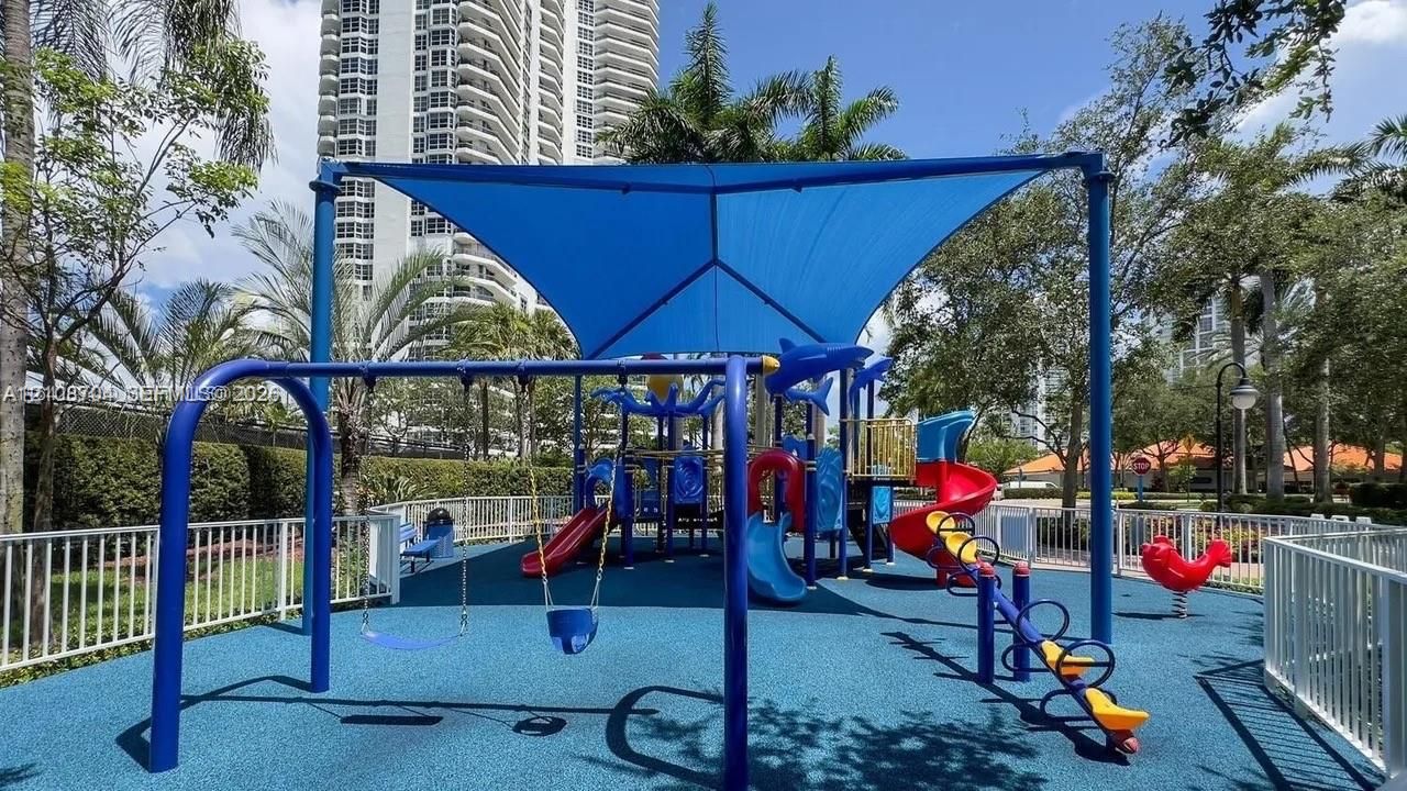 Playground facility featuring a blue shade canopy, integrated play structure, multi-colored slides, swing set, and rubberized ground surfacing