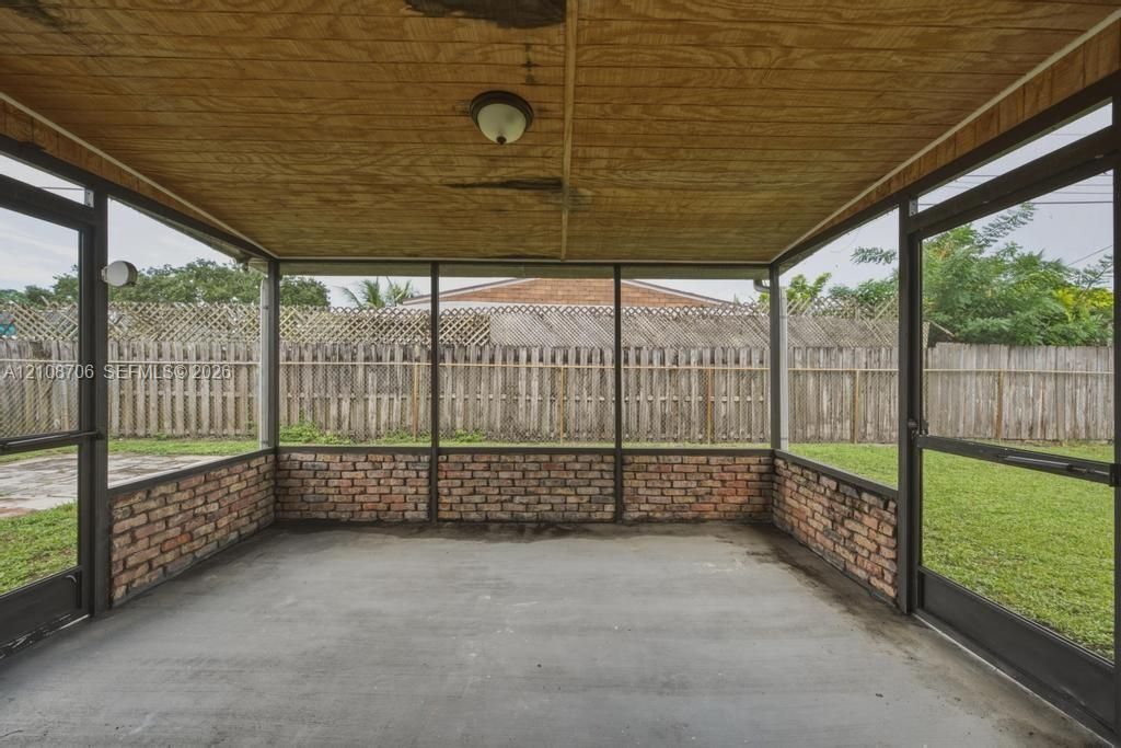 Screened-in porch featuring exposed brick wall segments, concrete flooring, wood-paneled ceiling, and two metal-frame screen doors