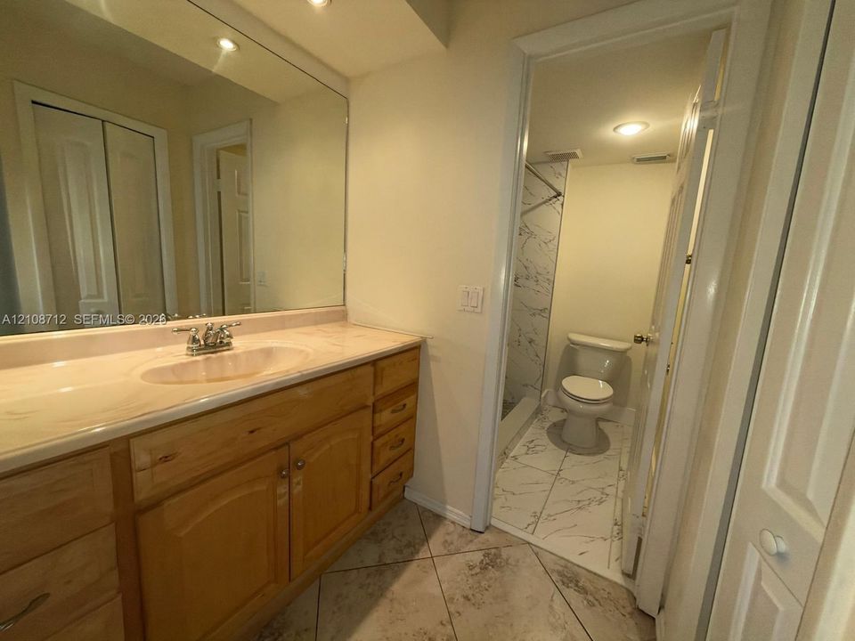 Bathroom featuring wood-finish cabinetry, an expansive wall-mounted vanity mirror, ceramic tile flooring, and a separate water closet area with patterned tile surrounds