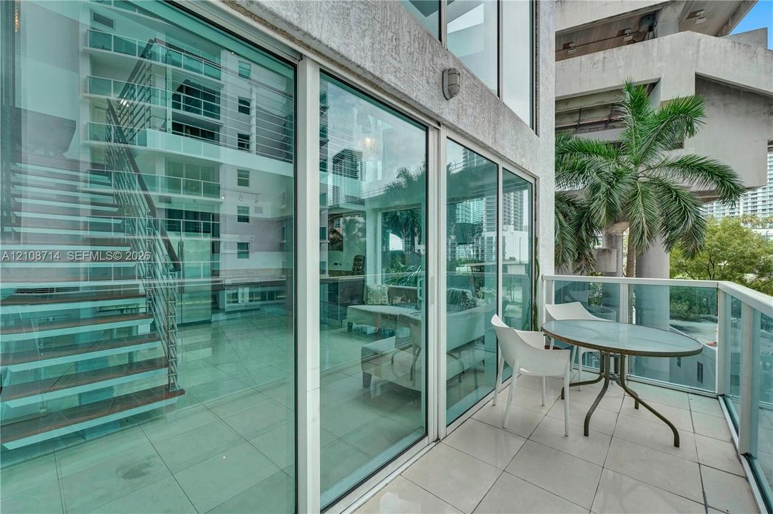 Private balcony featuring tile flooring and a glass-paneled railing, floor-to-ceiling glass wall, and interior staircase with wood-finish treads and metallic railing