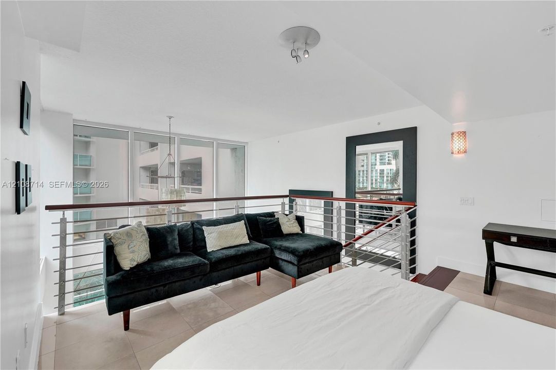 Open-concept mezzanine featuring metal horizontal-rail balustrades with a dark wood handrail, large floor-to-ceiling windows, tile flooring, and integrated wall-mounted lighting
