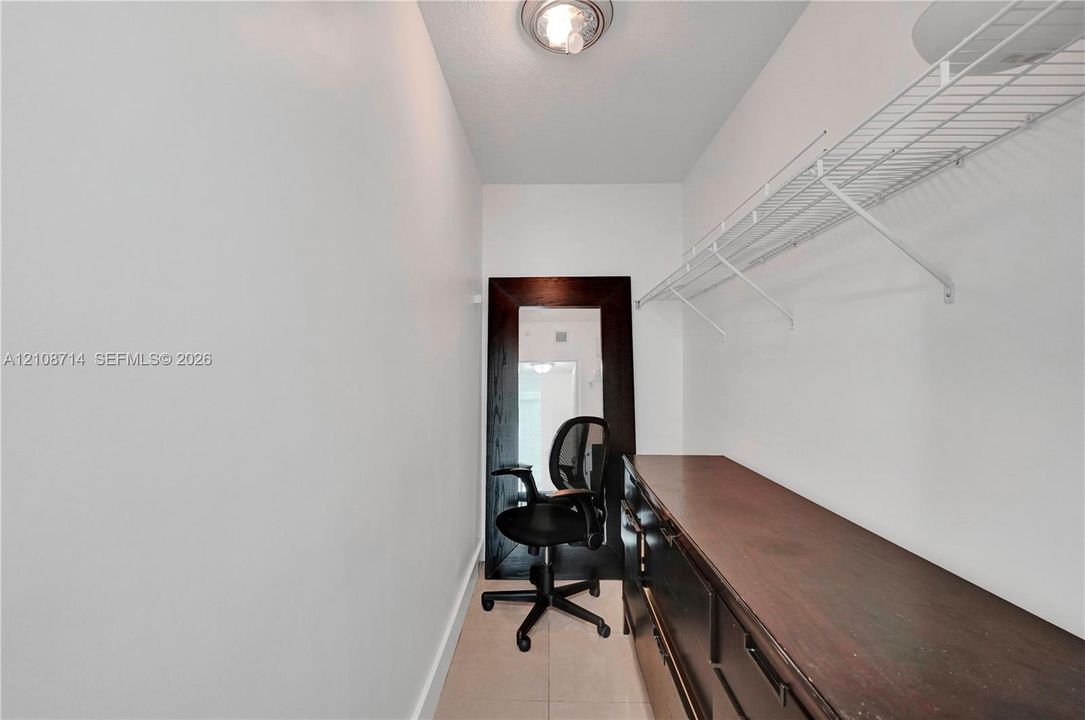 Storage space featuring tile flooring, white walls, overhead lighting, wire shelving, and dark wood-finish cabinetry