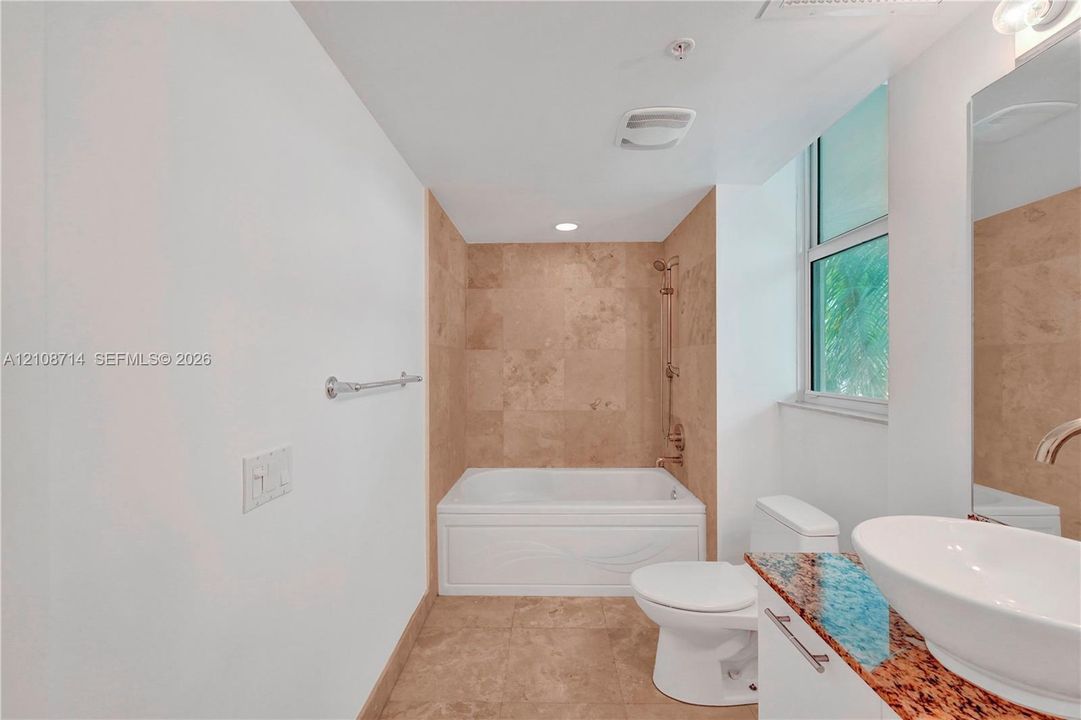 Bathroom featuring a white soaking tub with a tiled surround, stone-finish vanity countertop, vessel sink, and large wall-mounted mirror