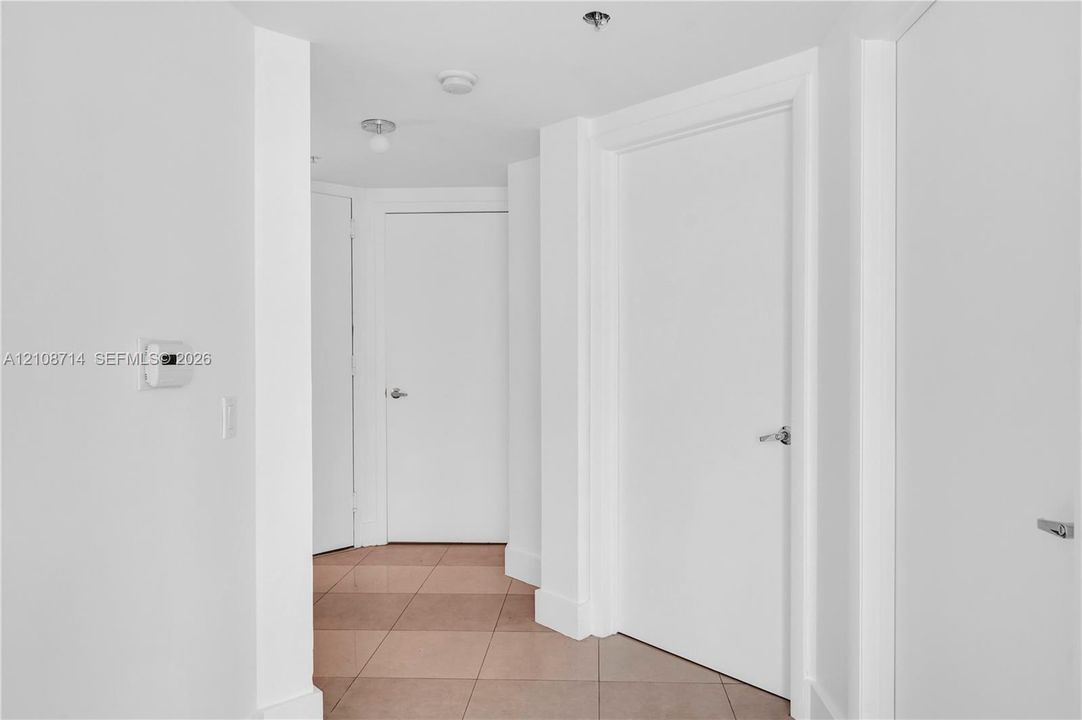 Interior hallway featuring neutral-toned tile flooring, solid core doors with brushed metal hardware, and recessed lighting