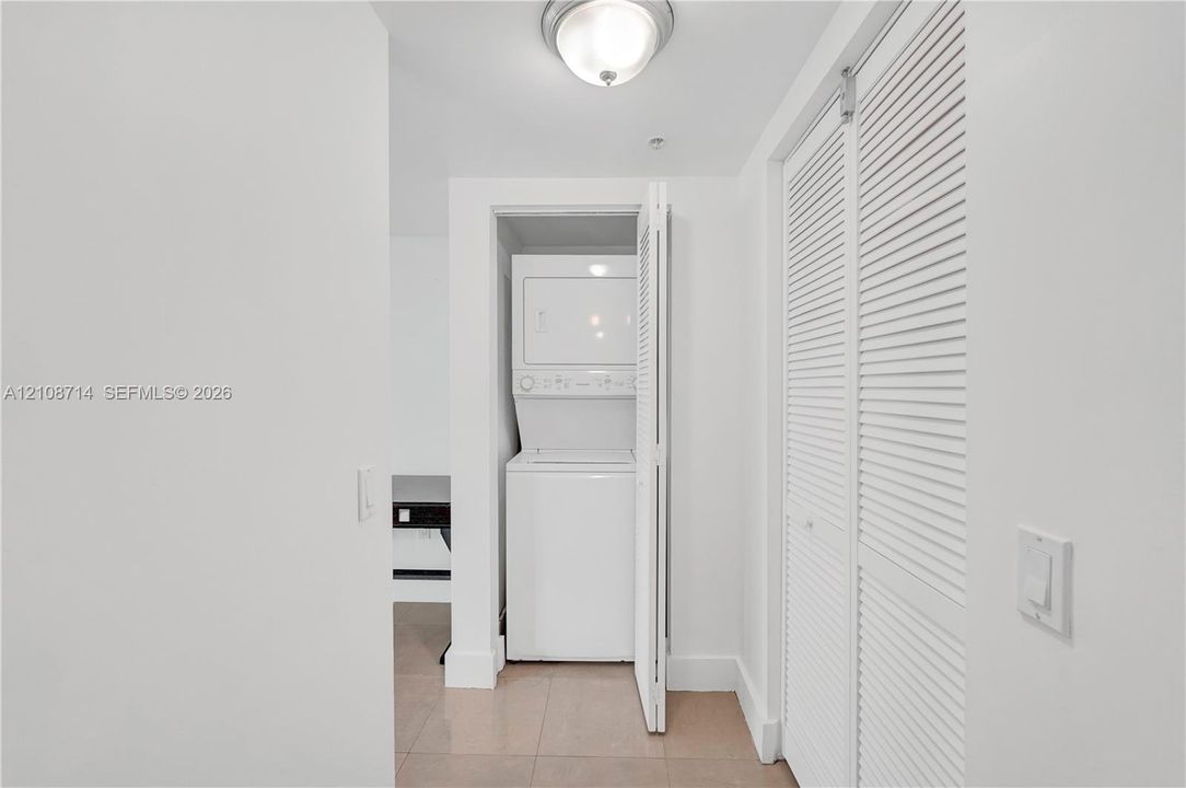 Stacked laundry unit, louvered closet doors, and flush-mount overhead lighting