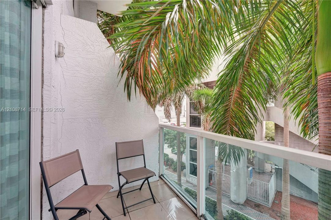 Private balcony featuring textured stucco walls, large-format tile flooring, and a glass-paneled railing