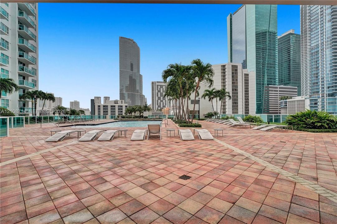 Terrace area featuring paver flooring, an in-ground swimming pool, glass perimeter railing, and palm tree landscaping