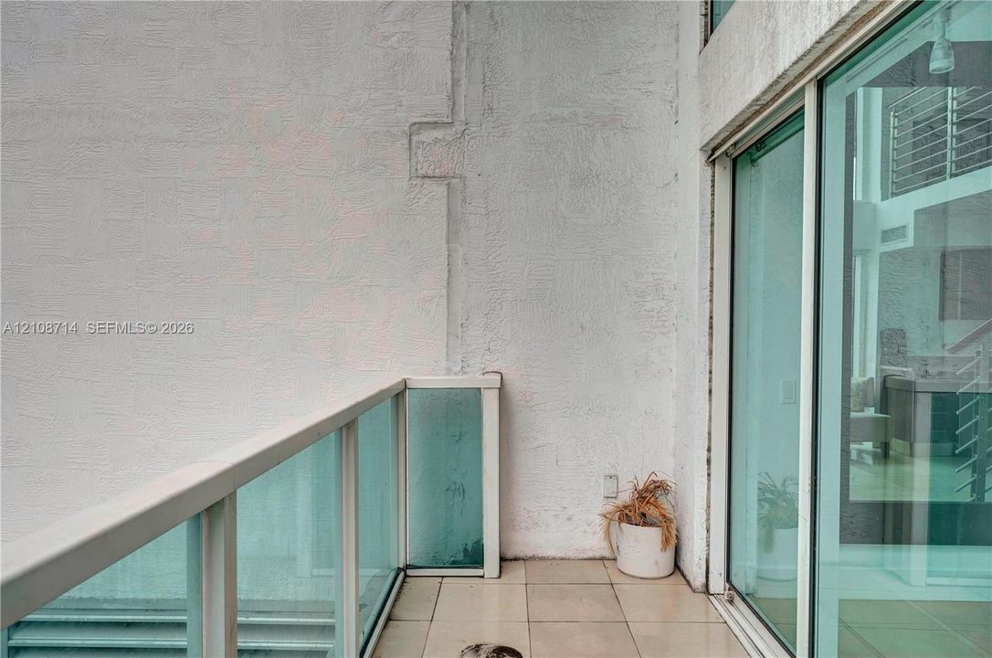 Outdoor terrace featuring large-format neutral floor tiling, a glass panel railing with a white frame, and full-height sliding glass doors
