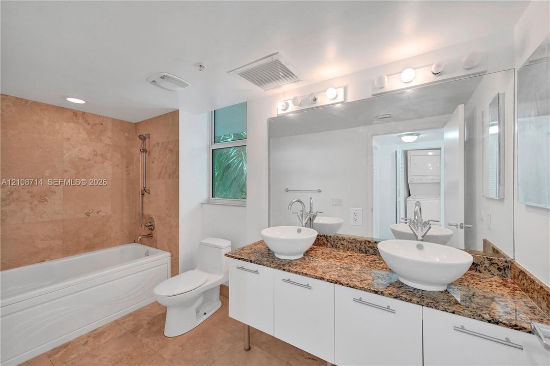 Bathroom featuring a floating vanity with dual vessel sinks, stone-finish countertops, tiled shower surround with a handheld showerhead, and a full-width wall mirror