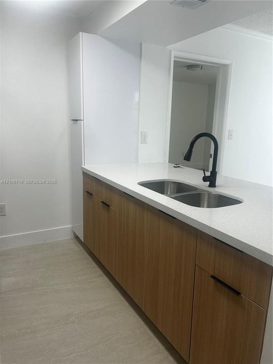 Kitchen featuring wood-finish cabinetry, white stone-surface countertops, a stainless steel dual-basin undermount sink, and a matte black gooseneck faucet