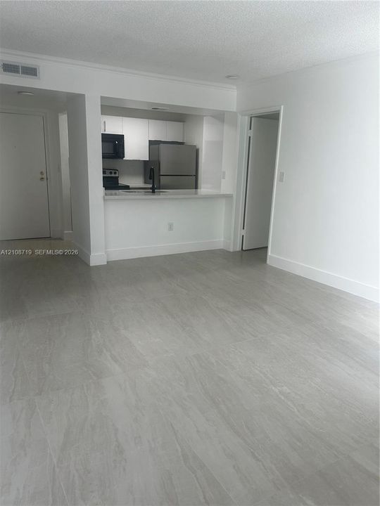 Open-concept living space featuring large-format tile flooring, white cabinetry, a breakfast bar, and stainless steel appliances