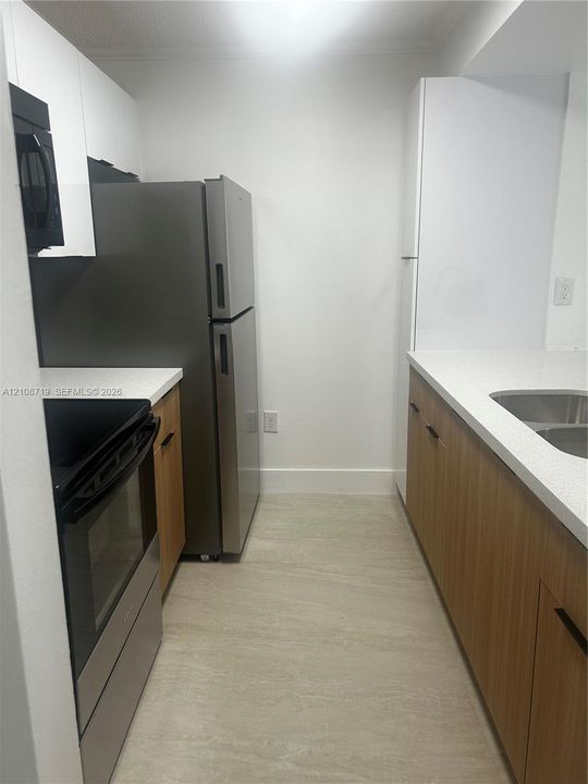Kitchen featuring stainless steel appliances, light wood-finish cabinetry, white stone-composite countertops, and neutral tile flooring