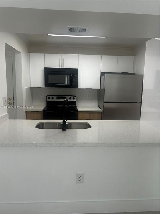 Kitchen featuring white flat-panel cabinetry, quartz countertops, stainless steel appliances, and a dual-basin undermount sink with a matte black faucet