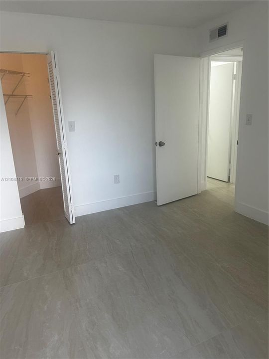 Neutral-toned tile flooring, white interior doors, and a walk-in closet with integrated wire shelving