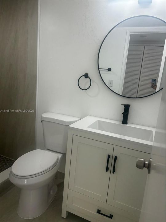 White vanity cabinet featuring a rectangular basin, matte black faucet, and matching cabinet hardware, accented by a circular wall mirror and circular towel ring