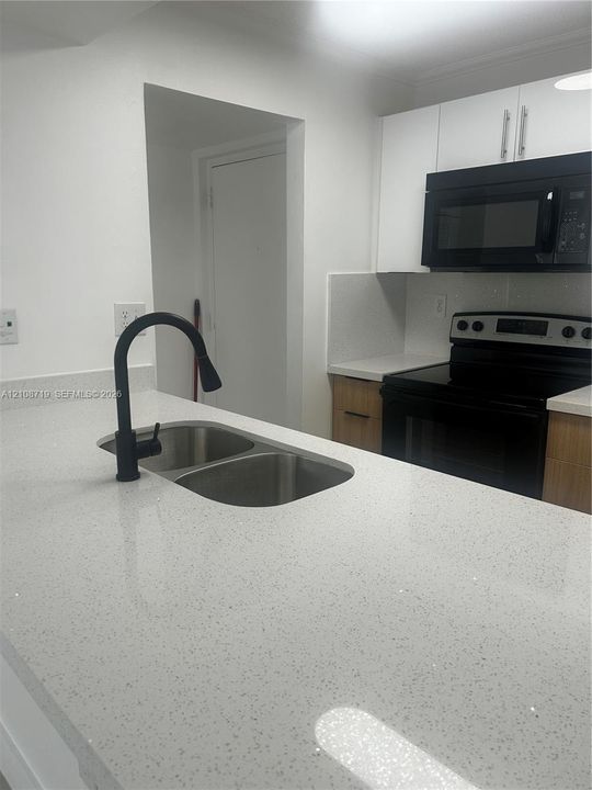 Kitchen featuring a stone-composite countertop, dual-basin stainless steel sink with a matte black pull-down faucet, flat-panel wood-tone cabinetry, and black appliances