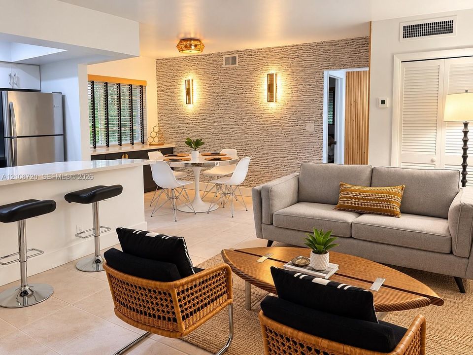 Open-concept interior featuring textured stone-look accent wall, dual vertical wall-mounted sconces, breakfast bar with integrated cabinetry, tile flooring, and louvered closet doors