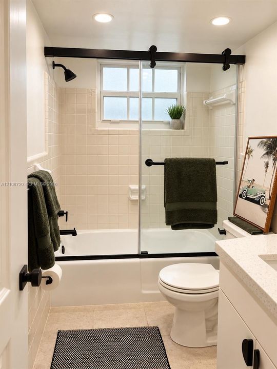 Bathroom featuring a shower-tub combination, sliding glass door with matte black hardware, tile wall surround, and vanity with a light-toned countertop