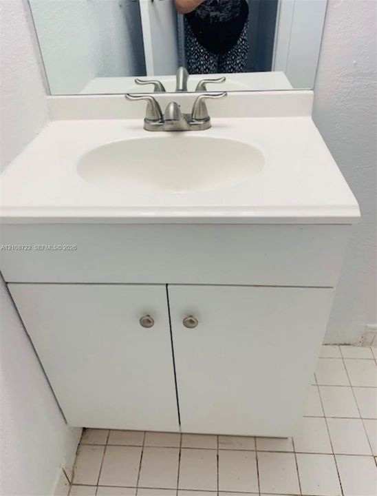 White vanity cabinet with integrated basin, polished metal dual-handle faucet, and rectangular wall-mounted mirror