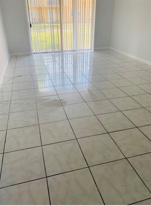 Large-format square tile flooring, vertical window blinds, and sliding glass door
