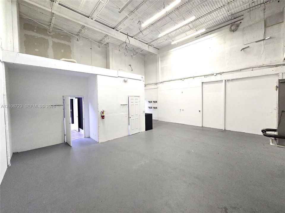 Industrial interior featuring high ceilings, exposed structural steel, expansive open floor plan, gray concrete flooring, and linear LED lighting